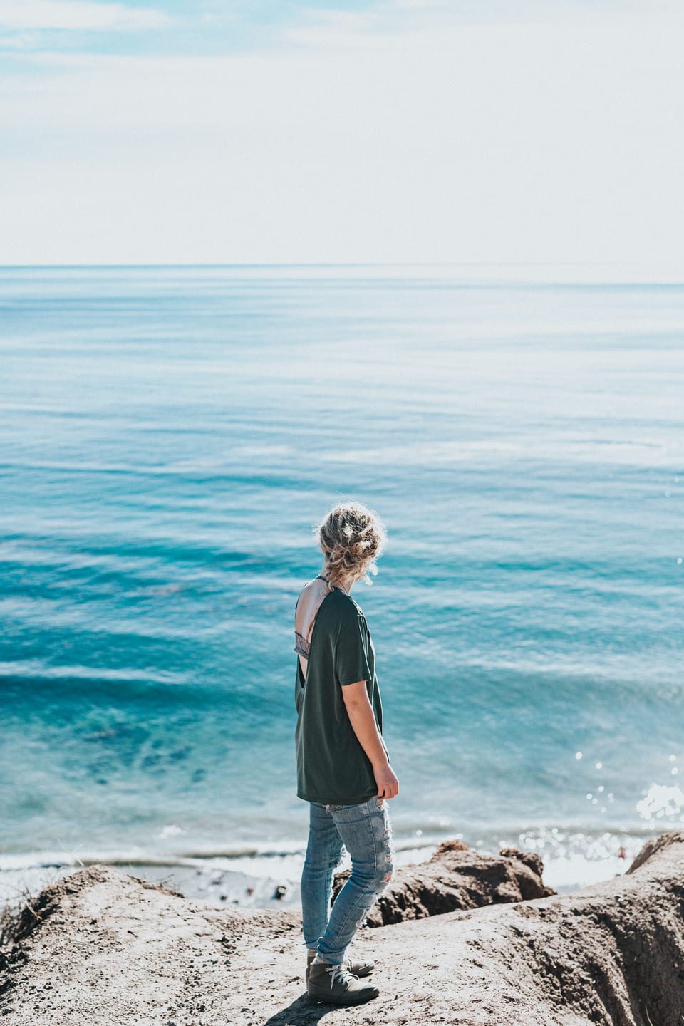Jeune femme de dos sur des rochers regardant la mer